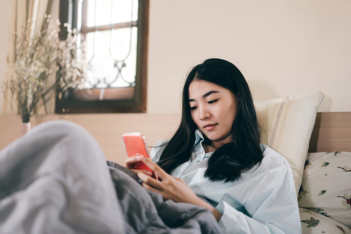 Young woman resting in bed, scrolling through her phone.